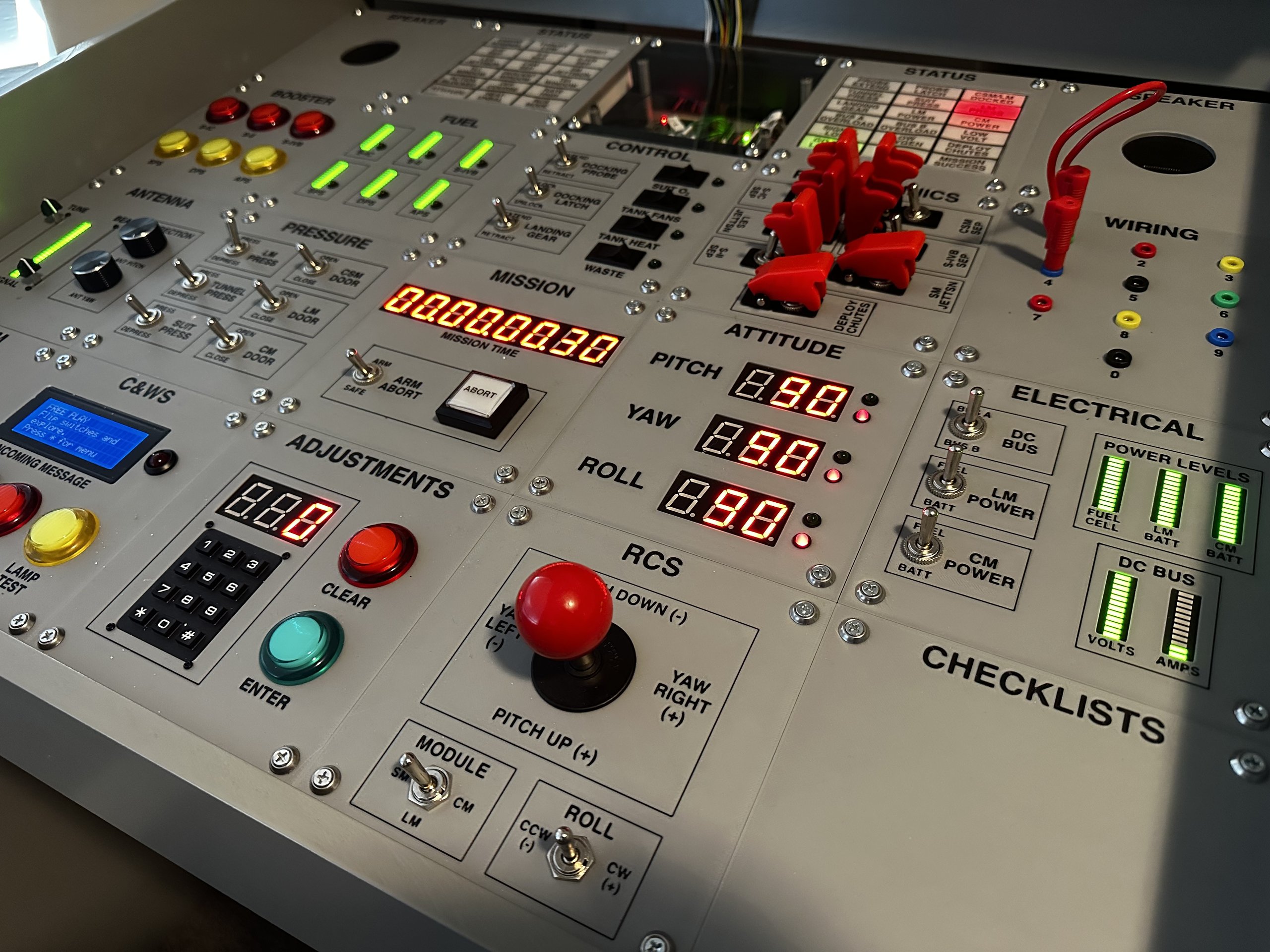 Close-up of the Apollo simulator control panel with lit displays, arcade buttons, toggle switches, and a joystick