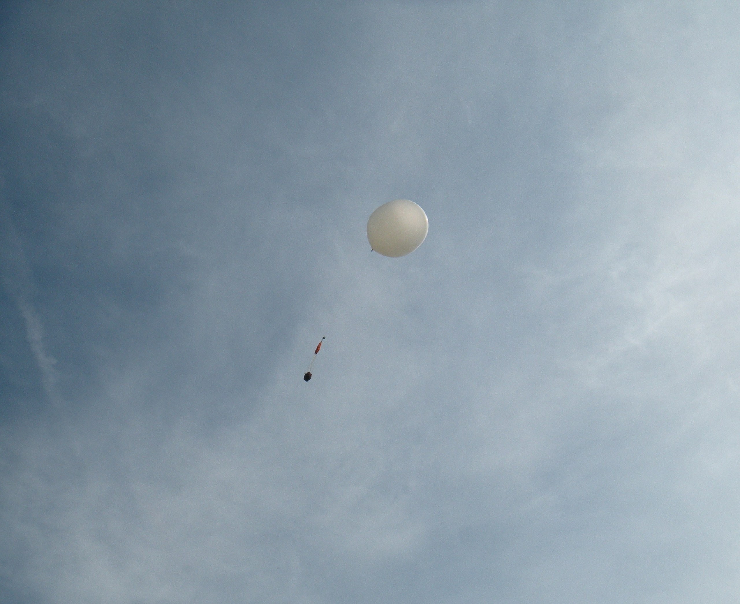 Weather balloon ascending into a hazy blue sky with the payload and parachute hanging below