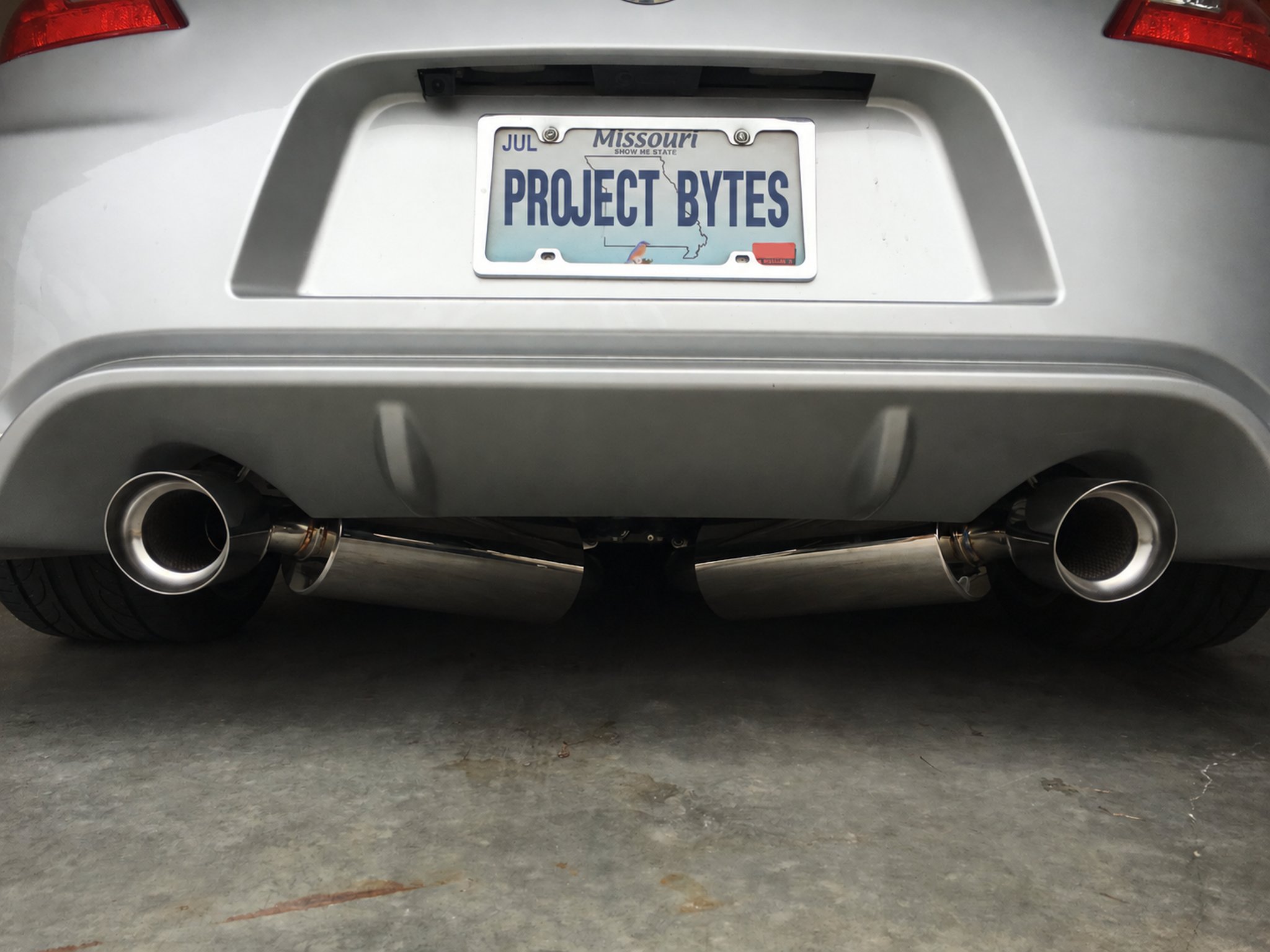 Rear of a silver Nissan 370Z showing the exhaust, with a Project Bytes license plate